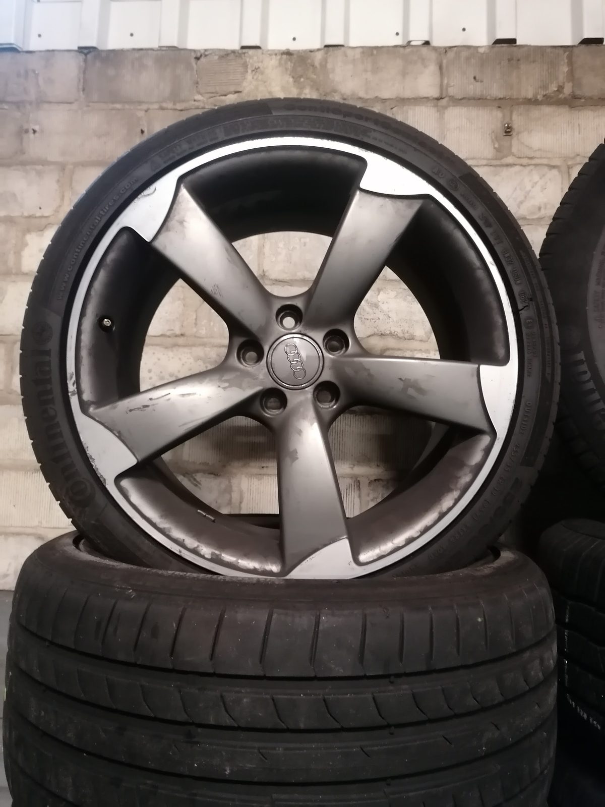A gunmetal five spoke alloy wheel resting on a stack of tyres